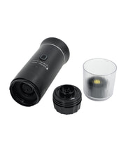 Black espresso maker disassembled showing main unit, detachable components, and transparent collection cup separated